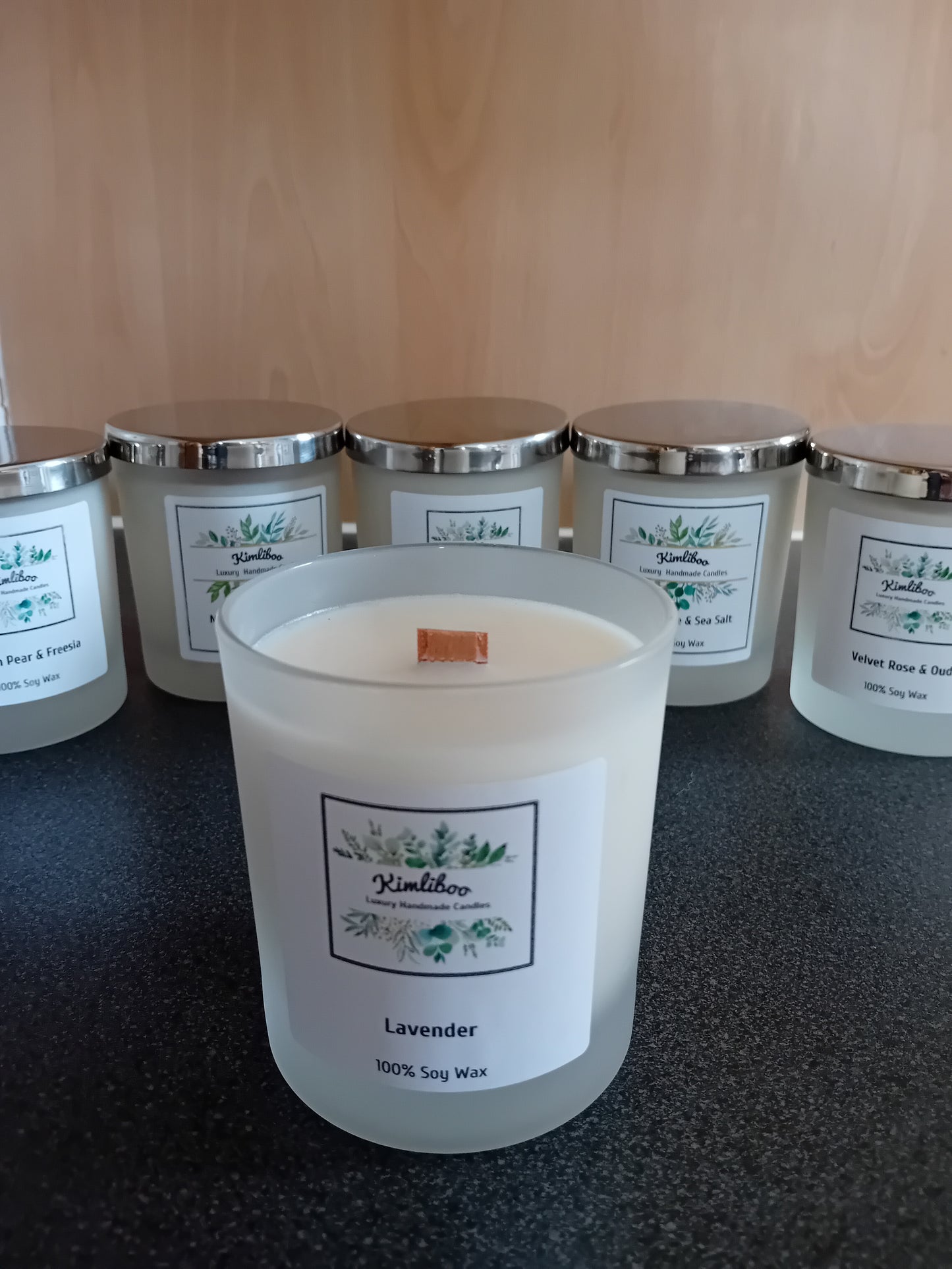 Frosted jar of lavender scented wax with a wood wick and a label, on a dark surface.