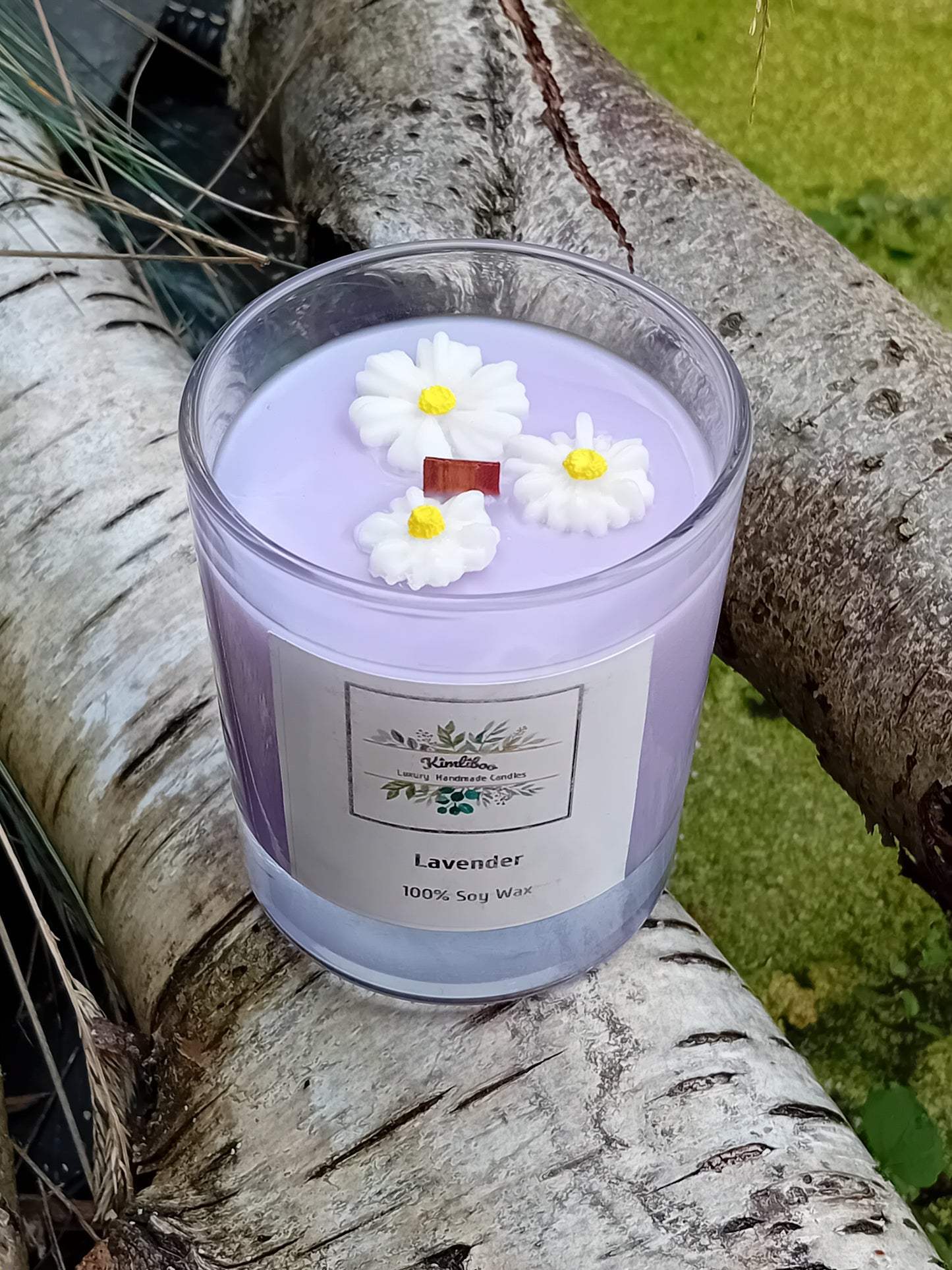 Lilac candle with daisy decorations on a tree branch