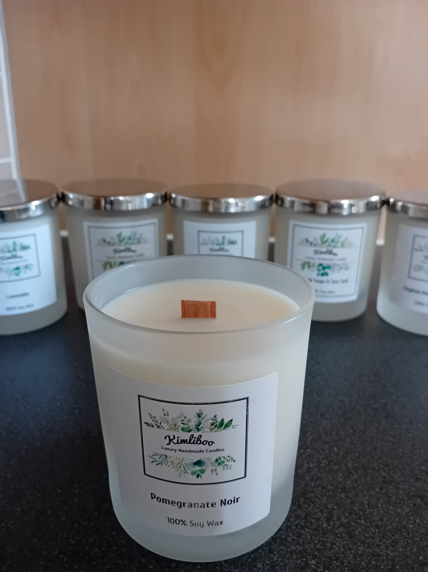 Frosted jar of pomegranate noir scented wax with a wood wick and a label, on a dark surface.