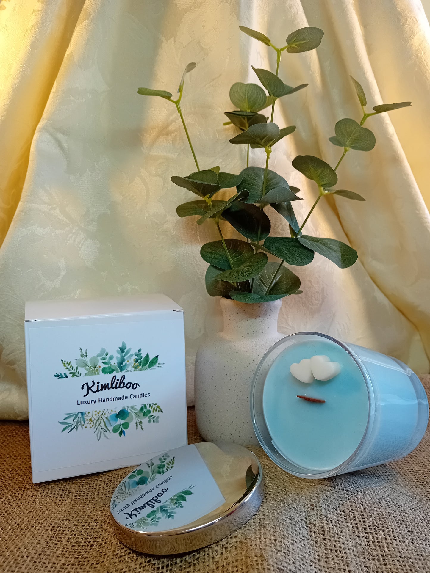 Wood Sage & Sea Salt fragranced light blue candle with wooden wick and two white heart-shaped ax decorations.