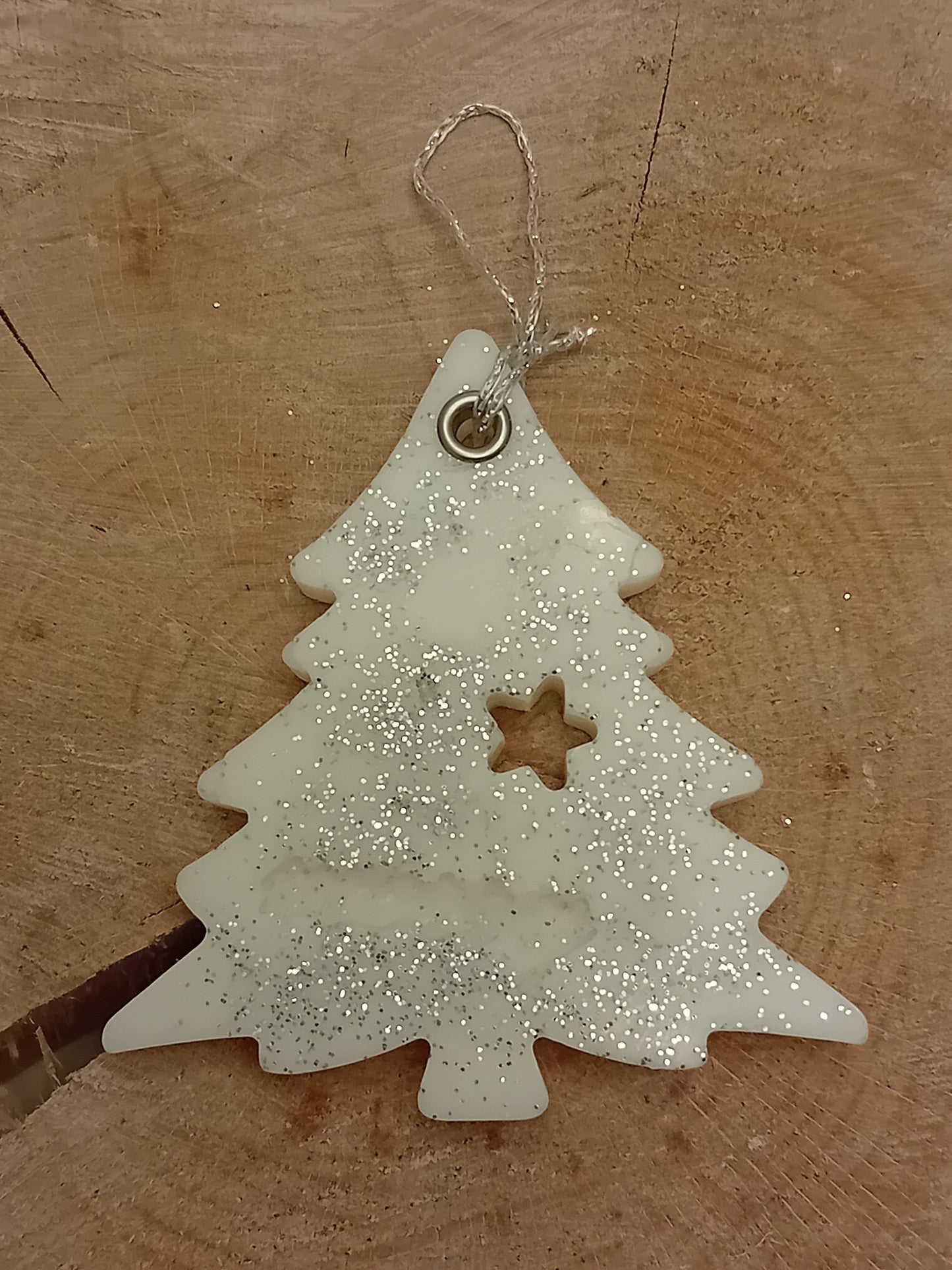 Christmas Tree shaped wax sachet decorated with a piece of crystallized ginger, a wax gingerbread man, pink peppercorns and silver glitter with a wooden log slice background.