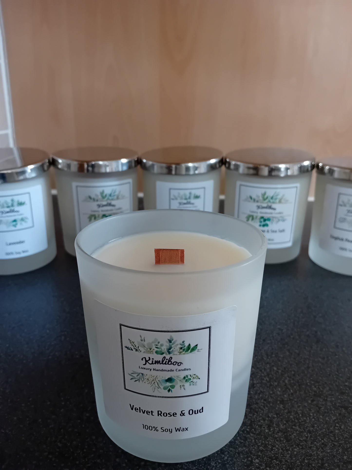 Frosted jar of velvet rose & oud scented wax with a wood wick and a label, on a dark surface.