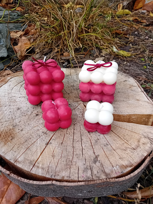 Deep red and white bubble shaped candles on a wooden log outdoors