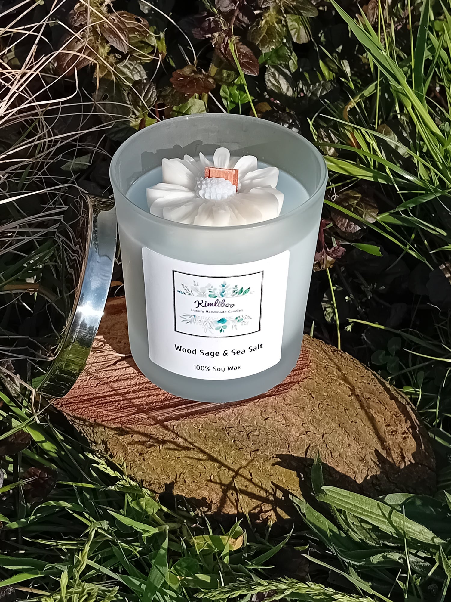 Wood Sage & Sea Salt fragranced blue candle in a 30cl frosted jar with wooden wick and a large daisy-shaped wax decoration. 