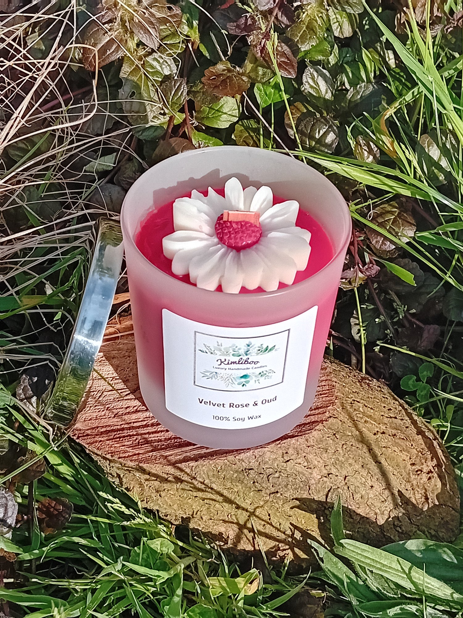 Velvet Rose & Oud fragranced  deep red candle in a 30cl frosted jar with wooden wick and a large daisy-shaped wax decoration. 