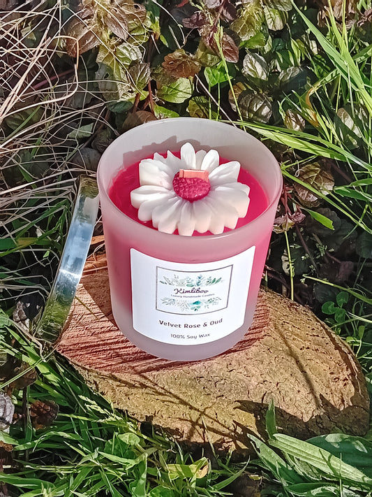 Velvet Rose & Oud fragranced  deep red candle in a 30cl frosted jar with wooden wick and a large daisy-shaped wax decoration. 
