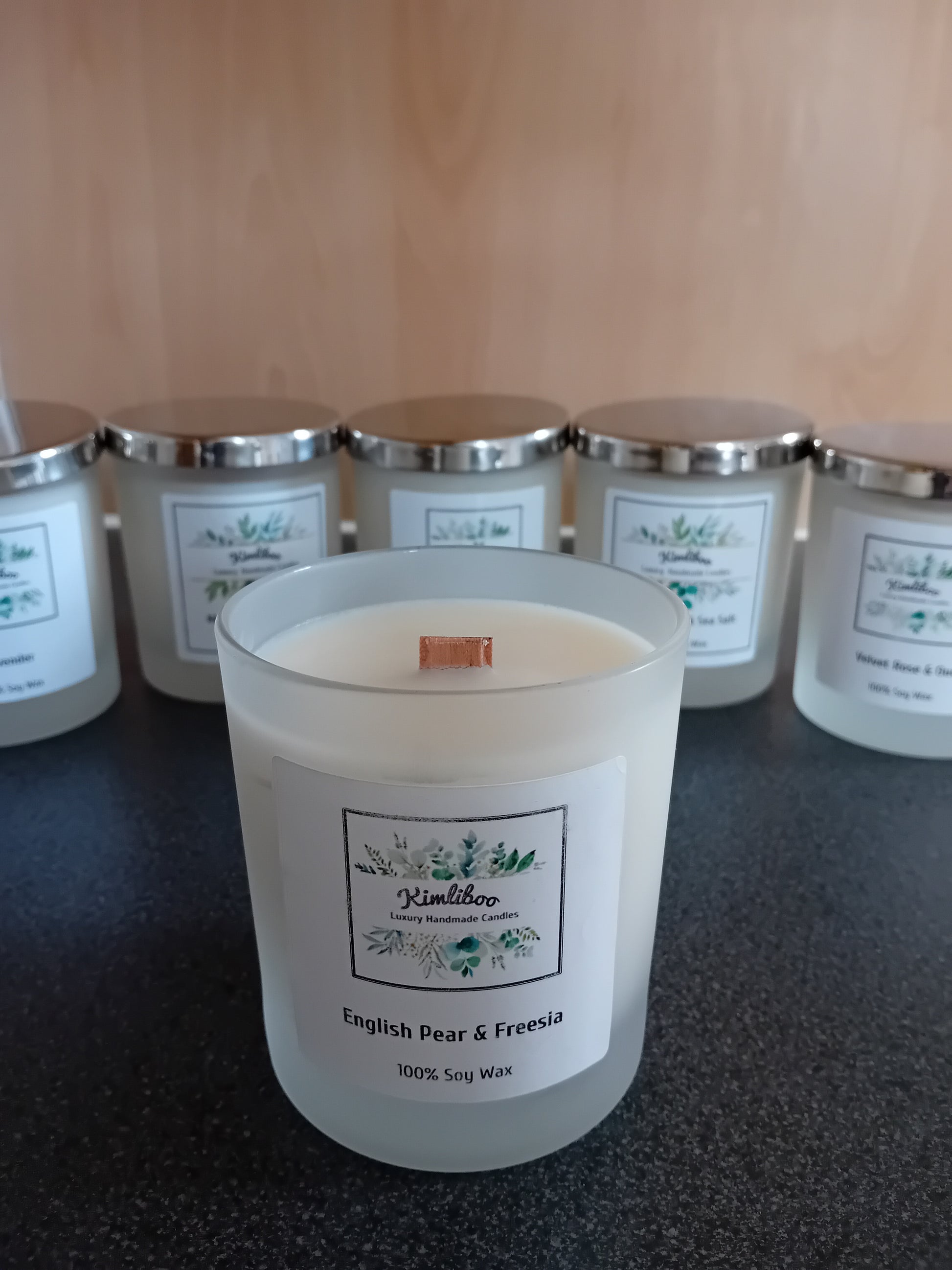 Frosted jar of English pear & freesia scented wax with a wood wick and a label, on a dark surface.