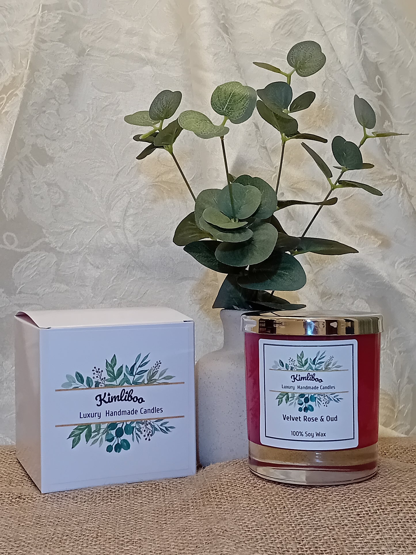 Deep red candle in a glass jar with a silver lid and a white gift box.