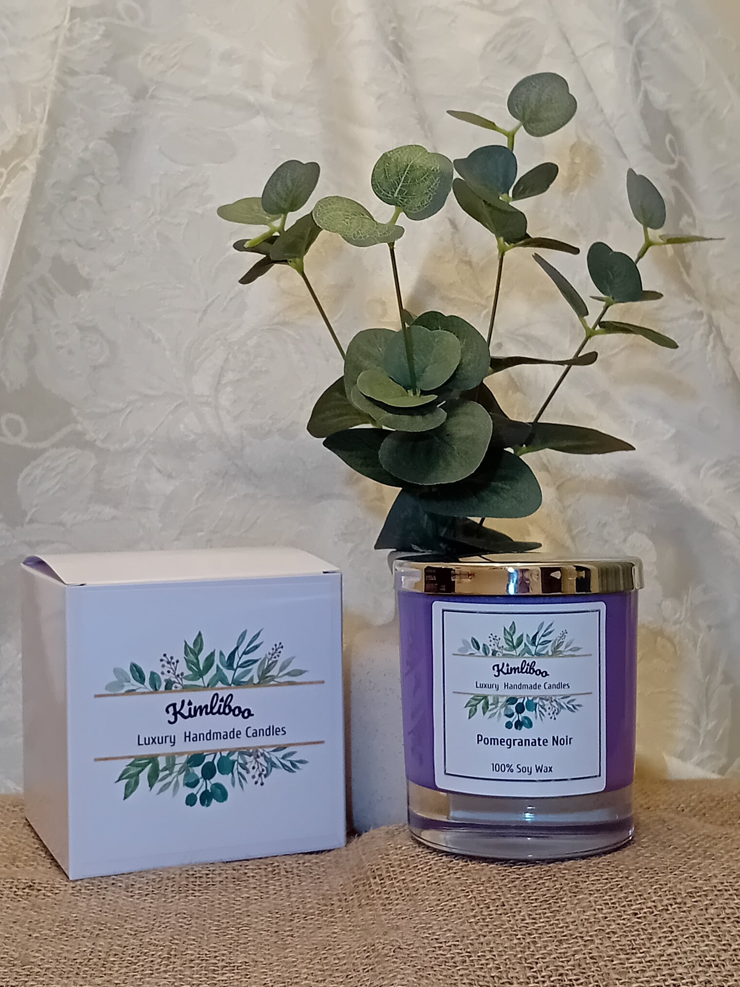 Purple candle in a glass jar with a silver lid, next to a white gift box.