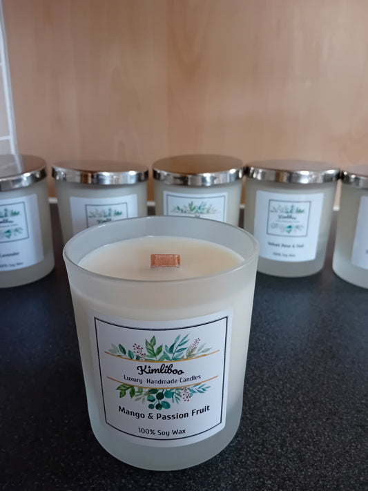 Frosted jar of mango & passion fruit scented wax with a wood wick and a label, on a dark surface.