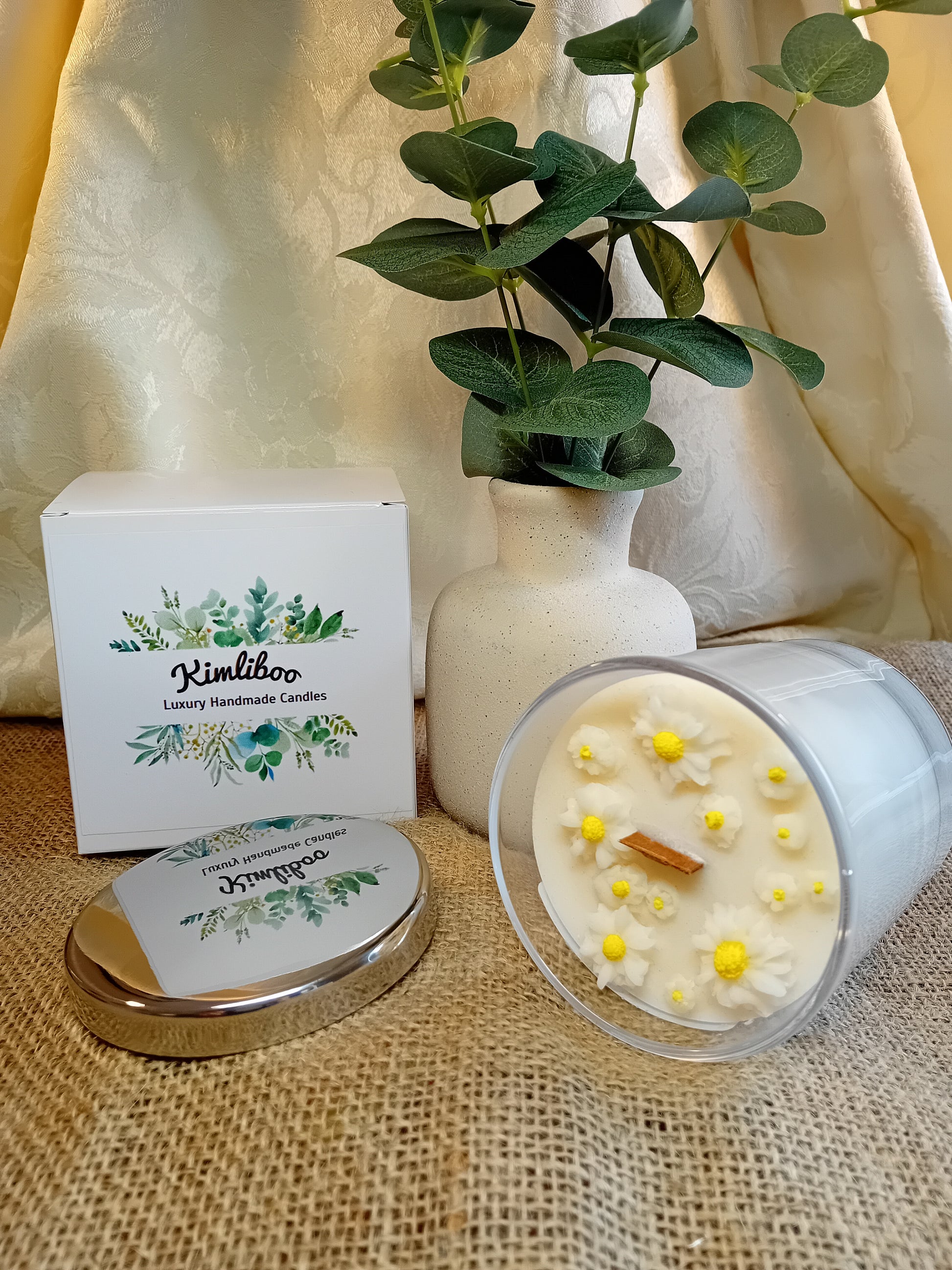 White fragranced candle with wooden wick and delicate daisy wax decorations.