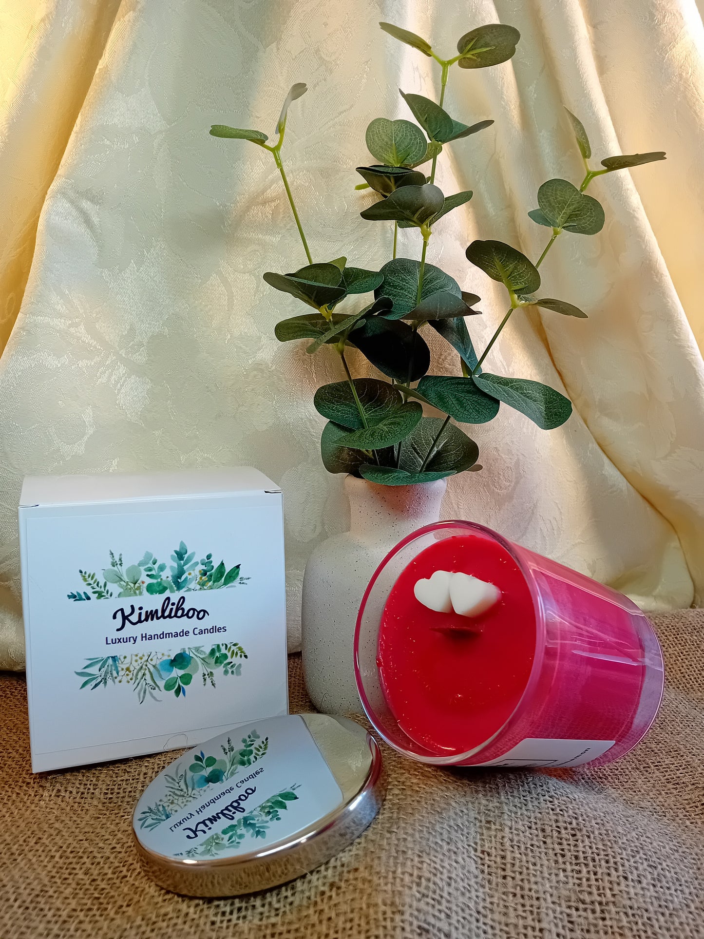 Cranberry, Orange & Cinnamon fragranced deep red candle with wooden wick and two white heart-shaped wax decorations.