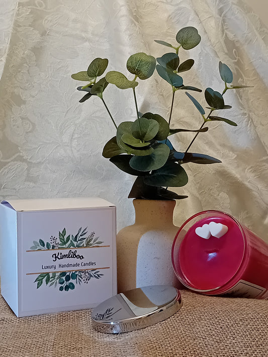 Deep red candle in a glass jar with two white mini-heart wax decorations, a silver lid and a white gift box.