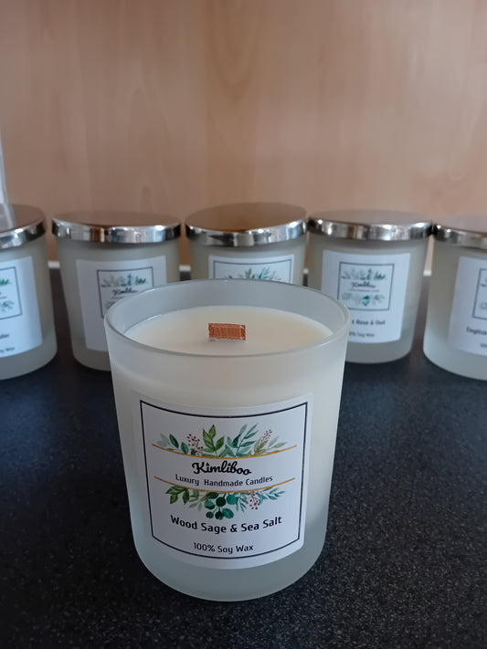 Frosted jar of wood sage & sea salt scented wax with a wood wick and a label, on a dark surface.